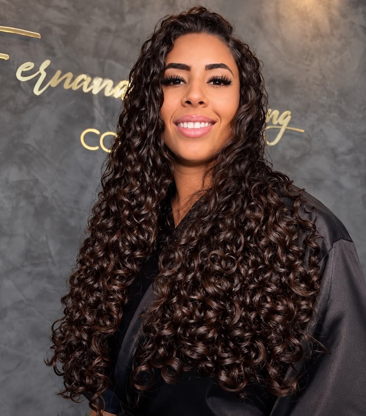 Cachos longos e definidos em cabelo castanho, em frente à parede do salão