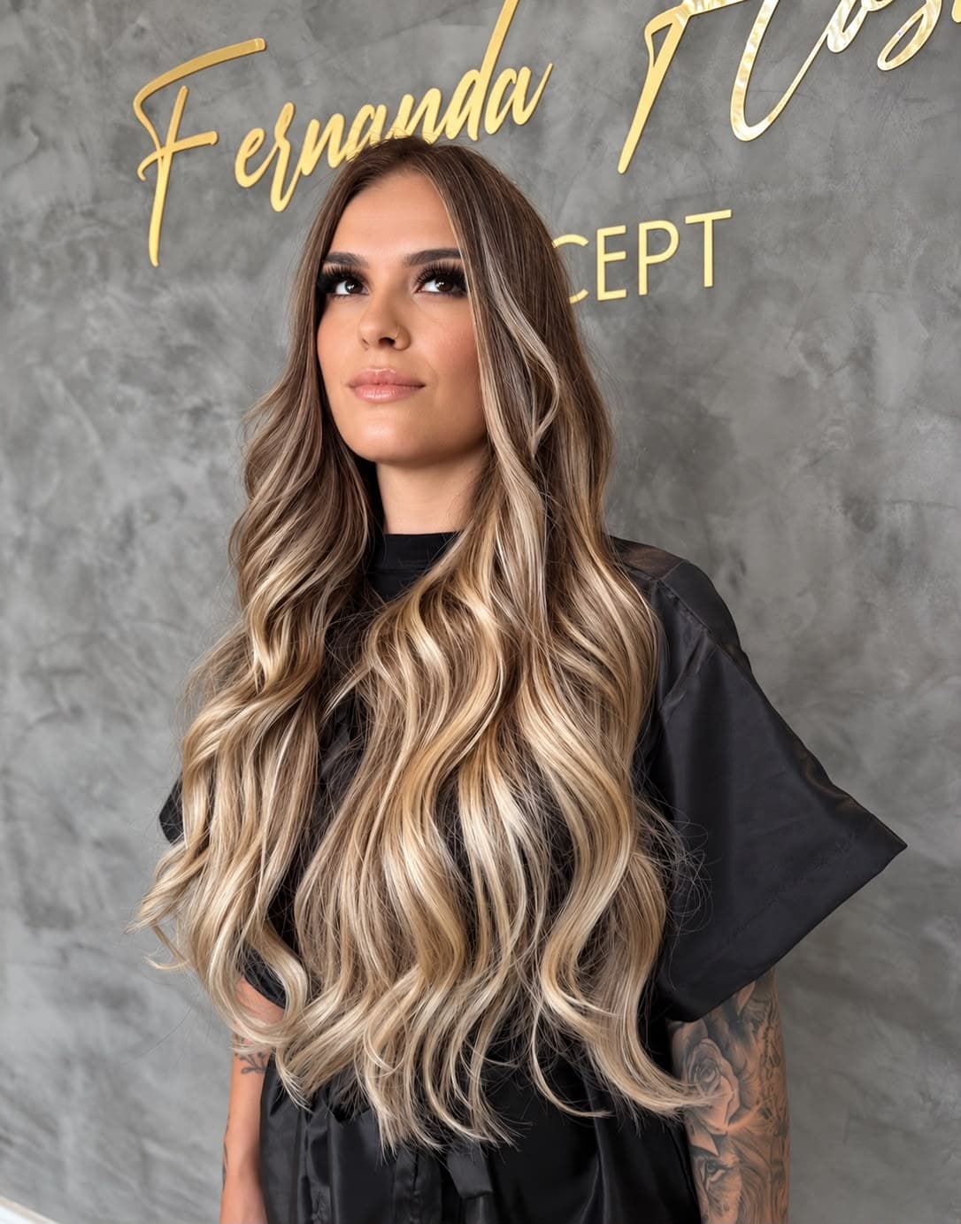 Mechas loiras em cabelo longo e ondulado, em frente à parede do salão